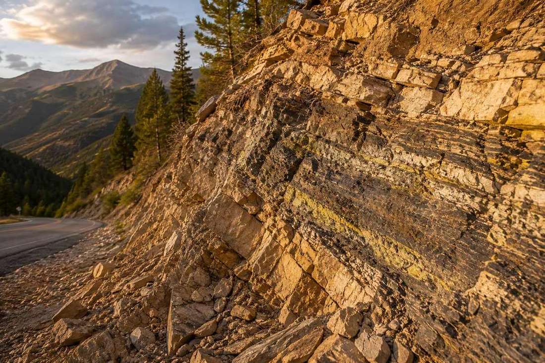 Fractured, uranium-bearing rock strata in a Roaring Fork Valley roadcut at golden hour